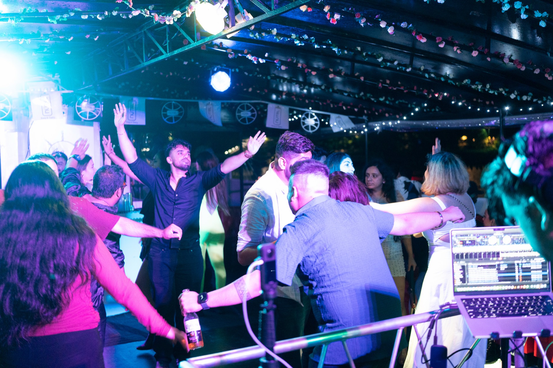 A packed dance floor under string lights and stage wash, DJ rig in the foreground